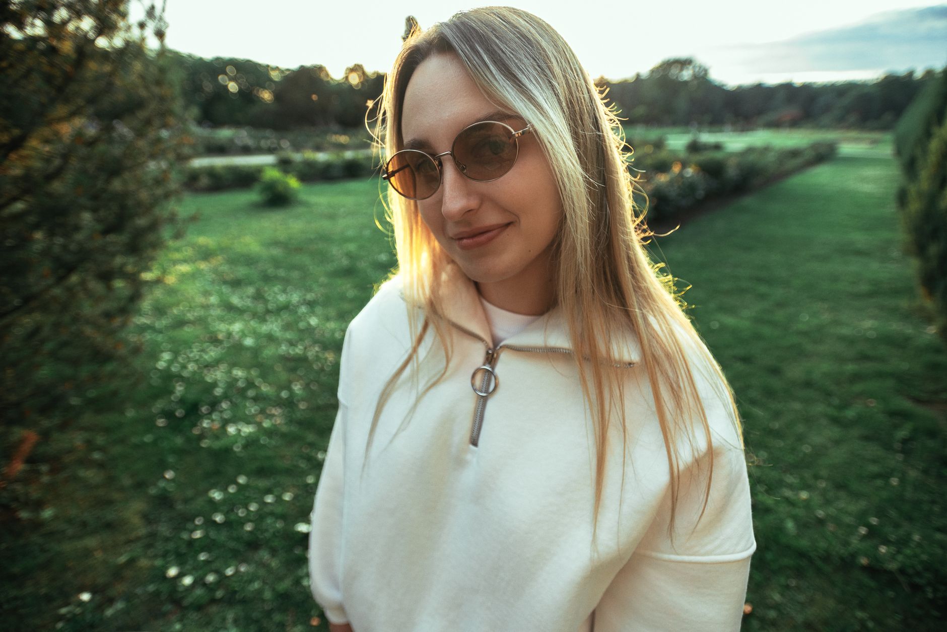 Mujer joven con gafas de sol de cristal marrón y montura metálica redonda en un parque