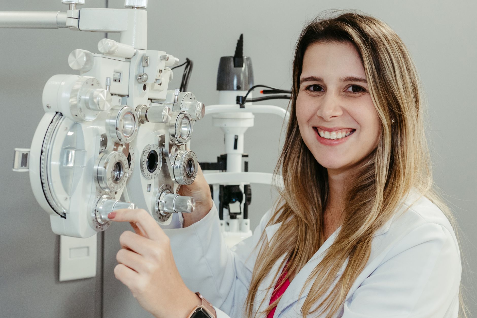 Óptica-optometrista sonriente junto a un foróptero en un gabinete de revisión visual