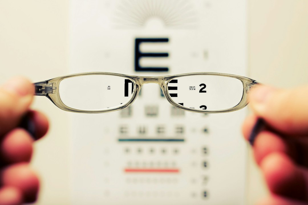 Manos sosteniendo unas gafas graduadas delante de un optotipo desenfocado